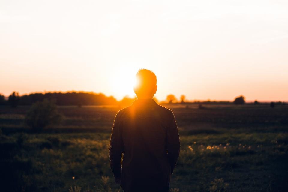 A man facing the sunrise over an open field
