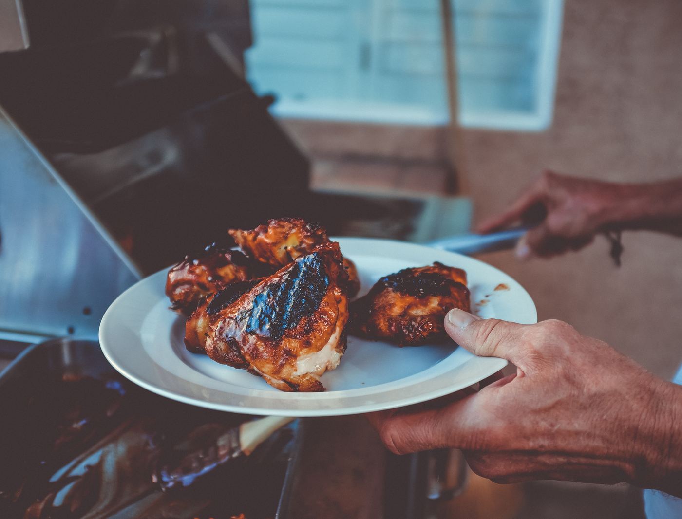 Hands serving a plate of grilled chicken